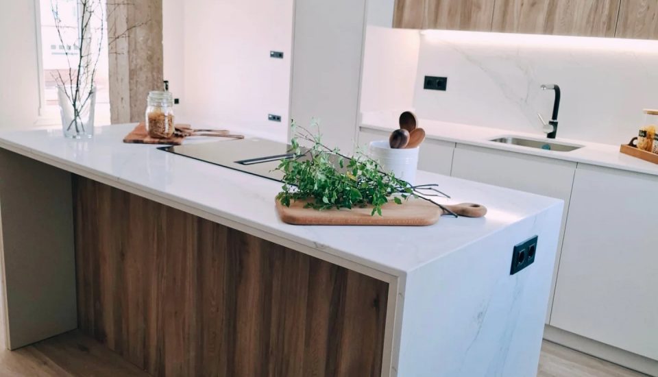 Cocina abierta con isla en cascada blanca y lateral de madera — reforma Izarte en Santurtzi