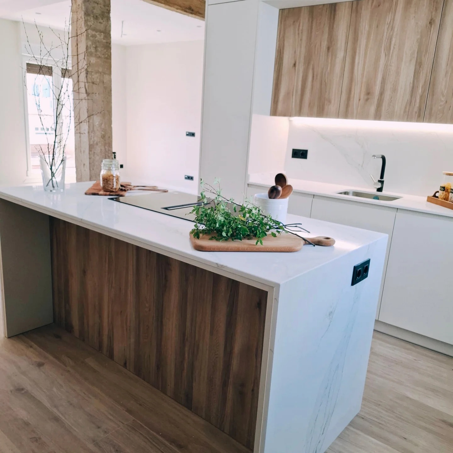 Cocina abierta con isla en cascada blanca y lateral de madera — reforma Izarte en Santurtzi